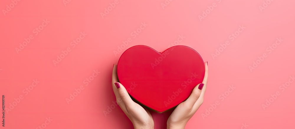 Poster a heart shaped closed red box is held by female hands on a pink background it creates a festive back
