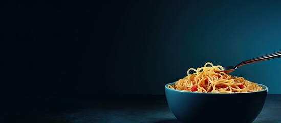A fork holds instant noodles on a dark blue bowl while copy space is available on the left side of the image