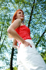 A girl in a red blouse and white jeans poses for the camera in nature. Joy, happiness, serenity. A girl poses for a photographer in nature.