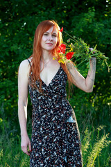 A girl with wild poppies enjoys the view from a hill near the river. Joy, happiness, serenity. Wild poppies by the river.