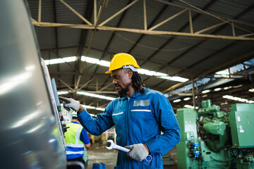 A man in a blue jumpsuit is working on a machine. He is wearing a yellow helmet and gloves