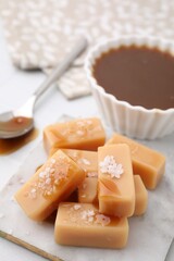 Delicious candies with sea salt and caramel sauce on white tiled table, closeup