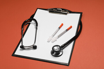 Stethoscope, syringes and clipboard on crimson background. Medical tools
