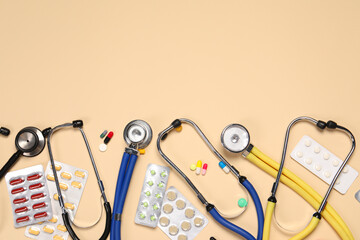 Stethoscopes and pills on beige background, flat lay. Space for text