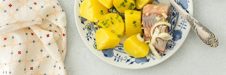 Delicious hearty fish dinners, boiled potatoes with pickled herring, top view, banner