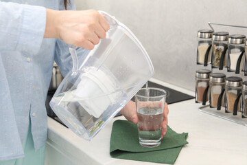 Woman pouring water from filter jug into glass in kitchen, closeup