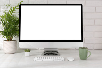 Fototapeta premium Office workplace with computer, cup, glasses, stationery and houseplant on light table near white brick wall