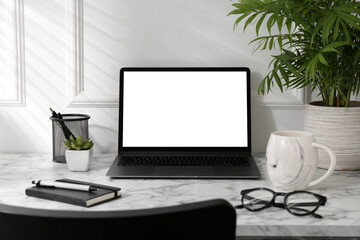 Office workplace with computer, glasses, cup and stationery on marble table near white wall