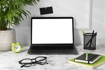 Office workplace with computer, glasses, houseplant and stationery on marble table near white wall
