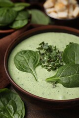 Delicious spinach cream soup with fresh leaves and microgreens in bowl on wooden table, closeup