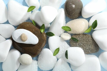 Spa stones and green leaves in water on light blue background, flat lay