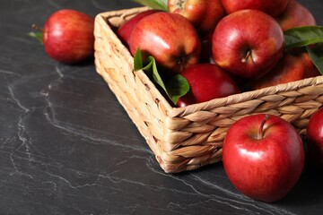 Fresh red apples and leaves in basket on dark grey table. Space for text