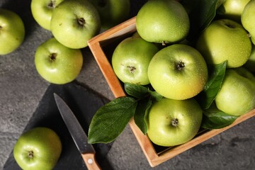 Ripe green apples with water drops, cutting board and knife on grey table, flat lay