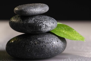Wet spa stones and green leaf on grey background, closeup