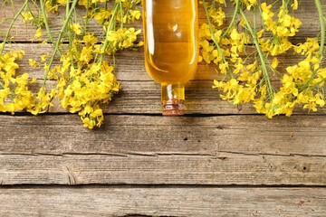 Rapeseed oil in glass bottle and beautiful yellow flowers on wooden table, flat lay. Space for text