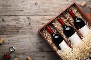 Box with wine bottles, corkscrew and corks on wooden table, flat lay. Space for text