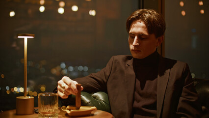 Young man with cigar in restaurant. Media. Young man in suit learns to smoke cigar in restaurant....
