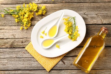 Rapeseed oil in gravy boats, bottle and beautiful yellow flowers on wooden table, flat lay