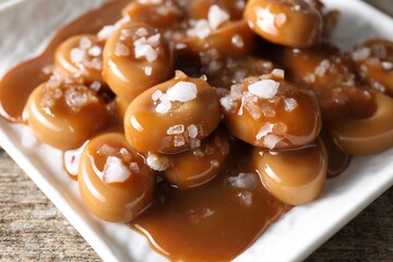Tasty candies, caramel sauce and salt on wooden table, closeup