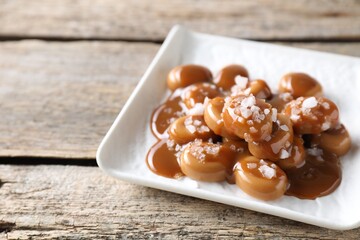 Tasty candies, caramel sauce and salt on wooden table, closeup. Space for text