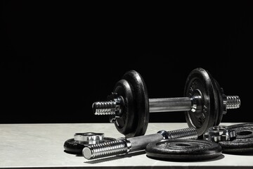 Barbell and parts of one on light table against black background. Space for text