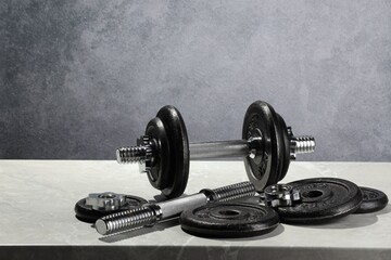 Barbell and parts of one on light table against grey background. Space for text
