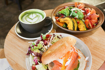 close up top shot of green tea latte with coffee art, salmon egg bagel and pumpkin salad in a cafe on a wooden table
