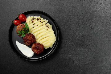 Fried cutlets with mashed potatoes, tomatoes and herbs. Black plate on a black background