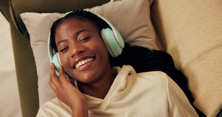 African woman, headphones and above on couch with smile, relax and peace with music in home living room. Girl, listening and happy for streaming, audio subscription and lying on lounge sofa in house