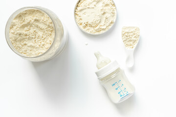 Milk for baby in a bottle with powdered milk in a spoon on white background, top view