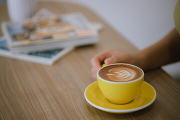 Close-up shot of hot latte coffee cup on wooden table in woman's hand in cafe