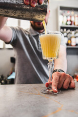 Close-up of a person pouring a yellow beverage into an elegant glass on a bar counter.