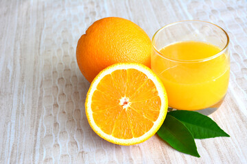 two oranges and a glass of orange juice on a table close up 