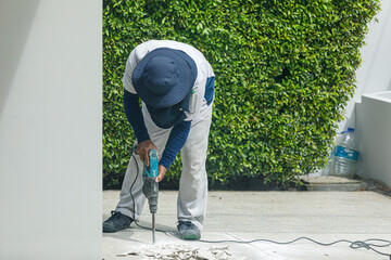 Builder worker with pneumatic hammer drill equipment breaking concrete at floor