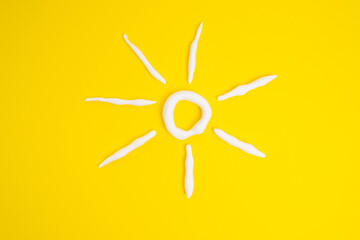 Sunscreen in the shape of a sun on a yellow background, white strokes of moisturizer. Skin health...