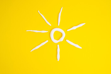 Sunscreen in the shape of a sun on a yellow background, white strokes of moisturizer. Skin health concept
