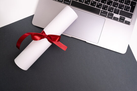 Diploma tied with a red ribbon on a laptop on a colored background. Education and science concept