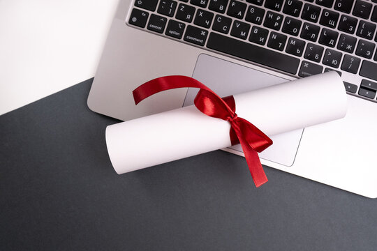 Diploma tied with a red ribbon on a laptop on a colored background. Education and science concept