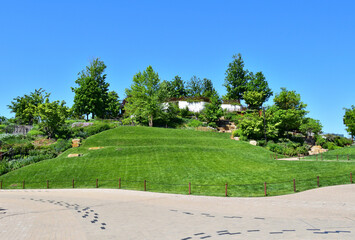 A lush green hillside with a white house in the distance in Little Island, NY. The hillside is covered in trees and grass