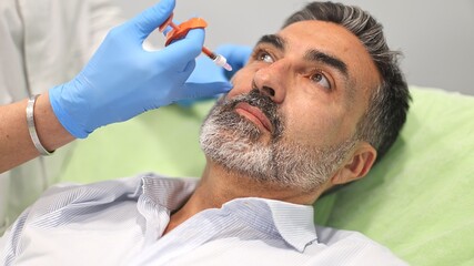 Fototapeta premium Doctor performing cosmetic injection on male patient's face at clinic