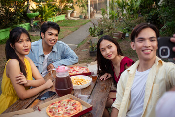 Four young Asian friends taking a selfie while enjoying a pizza picnic in the yard. Colleagues catching up over dinner.