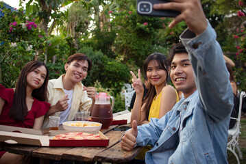 Four young Asian friends taking a selfie while enjoying a pizza picnic in the yard. Colleagues catching up over dinner.