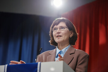 Confident woman in formalwear speaking in microphone while standing by tribune and sharing her...