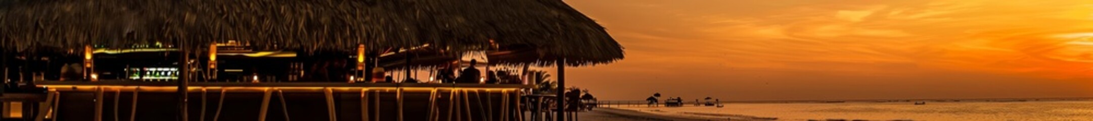 Obraz premium A beach bar with thatched roofs and tiki torches, serving tropical drinks to vacationers as they watch the sunset. The relaxed atmosphere and beautiful setting create a perfect summer evening.
