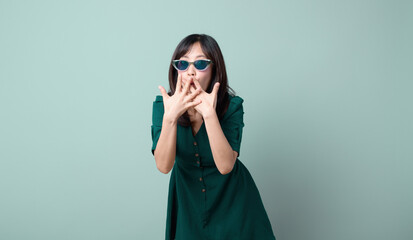 A shocked excited surprised asian woman 30s in green dress standing keeping mouth open spreading hands looking camera isolated on pastel green background studio portrait.