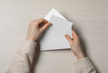 Woman taking card out of letter envelope at light wooden table, top view