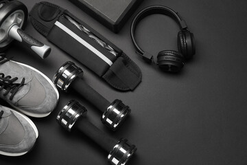 Sports equipment, headphones and sneakers on black background, flat lay. Space for text
