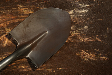 Metal shovel with fertile soil on dirty wooden surface, top view. Space for text