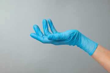 Doctor wearing light blue medical glove holding something on grey background, closeup