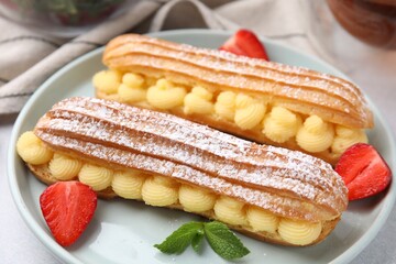 Delicious eclairs filled with cream, strawberries and mint on table, closeup